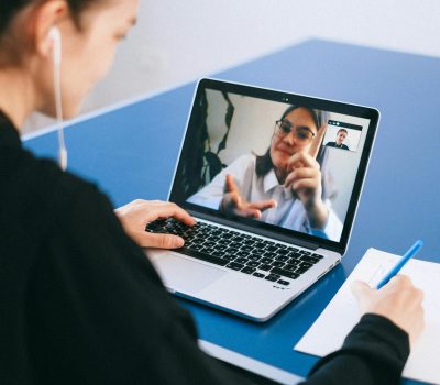 Woman participating in a virtual meeting, taking notes during a video conference on a laptop.
