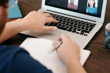 Person taking notes during a virtual meeting on a laptop screen with a diverse team.