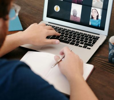 Person taking notes during a virtual meeting on a laptop screen with a diverse team.