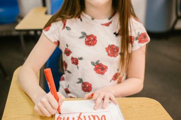 Young girl writing 'Stop Bullying' at desk, promoting kindness.